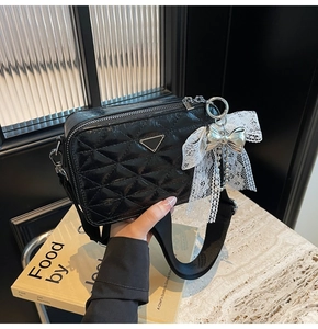 Detail of black quilted camera bag with lace bow pendant and wide canvas shoulder strap