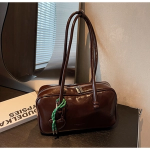 Détail d'un sac bowling en similicuir marron brillant avec breloque cœur et cordon vert