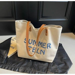 Détail d'un sac cabas en toile crème avec broderie bleue et anses en cuir marron