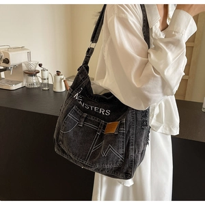 Detail der dunklen Denim-Tasche mit MONSTERS-Stickerei und Kontrastnähten