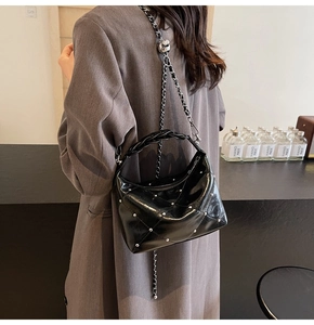 Close-up of black patent leather bag with silver studs and a chic woven handle