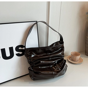 Macro detail of glossy pleated dark brown hobo bag with reflective patent finish texture