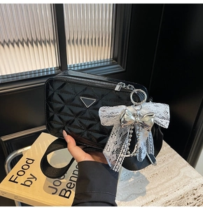 Detail of black quilted camera bag with silver triangle plaque and lace bow charm