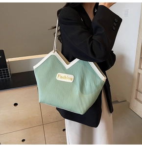 Detail of light green pleated tote bag with V-shaped opening and cream leather handles