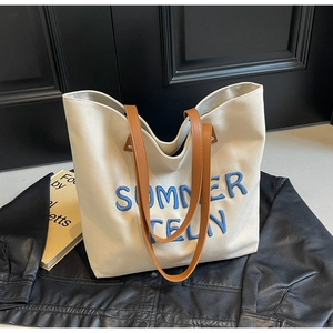 Détail d'un sac cabas en toile crème avec broderie bleue et poignées en cuir