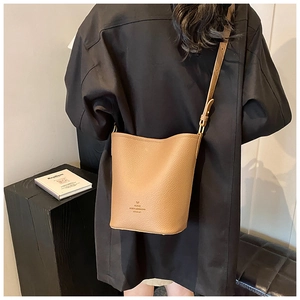 Detail view of a brown pebbled leather bucket bag styled as a crossbody on a model