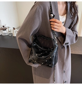 Detail of black quilted leather crossbody bag with silver rivets and metal chain strap