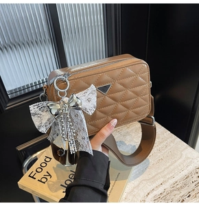 Detail of brown quilted camera bag featuring wide strap and lace bow charm accessory