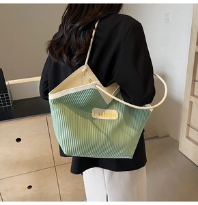 Detail of green pleated tote bag with cream shoulder strap and Fashion label
