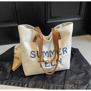 Détail du sac cabas en toile crème avec broderie bleue et poignées en cuir marron
