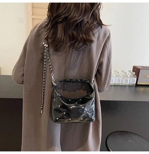 Detail of a black quilted hobo bag with silver studs and chain strap on a model