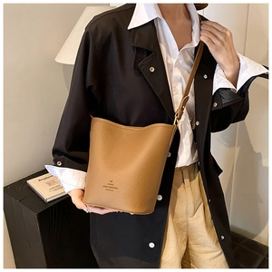 Chic brown leather bucket bag shown as a crossbody purse worn by a model in a stylish room