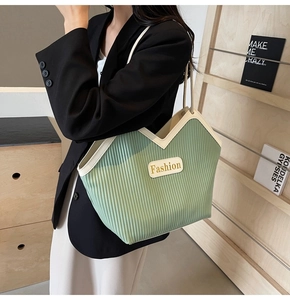 Detail of green pleated tote bag with cream leather trim and minimalist brand tag