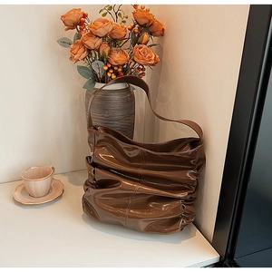 Detail of a dark brown glossy ruched shoulder bag with a vintage aesthetic design