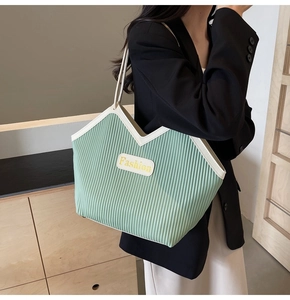 Green pleated tote bag with cream straps shown on model in a modern interior setting