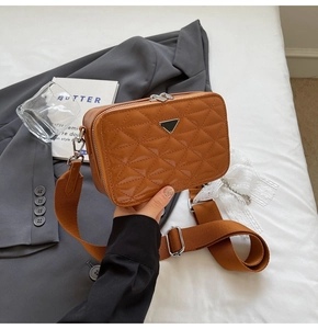 Close-up of caramel brown quilted leather camera bag with metallic triangular logo and strap