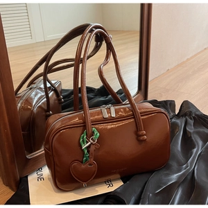 Détail d'un sac bowling en cuir marron brillant avec double zip et pendentif coeur