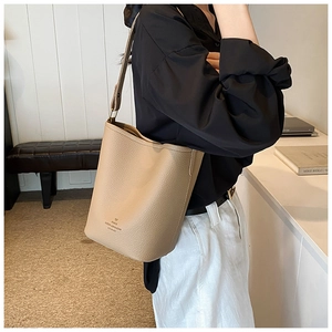Detail of a beige-brown leather bucket bag with wide strap on a model in a cozy home setting