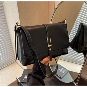 Detail view of black faux leather bag with rectangular gold buckle and long shoulder strap