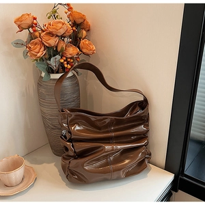 Detail of dark chocolate pleated leather shoulder bag with glossy texture in lifestyle setting