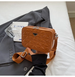 Detail of brown quilted camera bag with triangle metal logo and crossbody strap