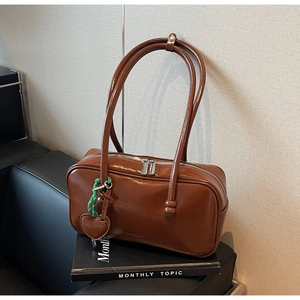 Détail d'un sac bowling vintage en cuir marron avec breloque cœur vert et zip argenté