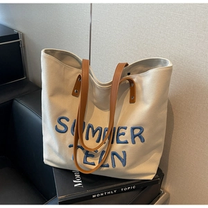 Gros plan sur le sac cabas en toile avoine avec broderie bleue et poignées en cuir brun