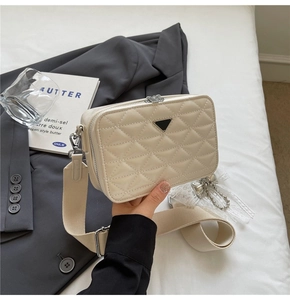 Detail of beige quilted leather camera bag with metallic triangle decor and wide strap
