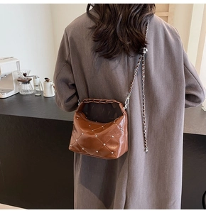 Rear view of model wearing brown quilted crossbody bag with silver studs and chain strap