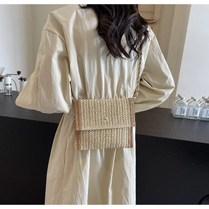 Dettaglio di una borsa a busta in paglia beige e marrone indossata da una modella in un caffè