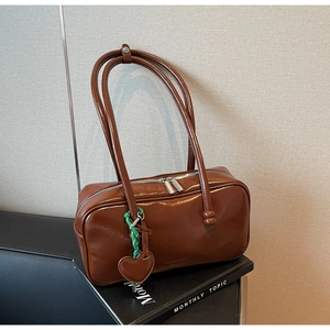 Détail du sac bowling rétro en cuir marron avec breloque cœur et accessoire tissé vert