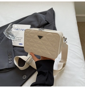 Detail of cream quilted camera bag with dual metal zippers and wide canvas shoulder strap