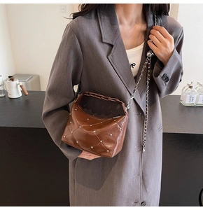 Close-up of brown quilted bag with silver rivets and metal chain strap on model