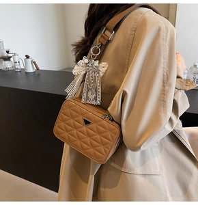 Close-up of brown quilted leather camera bag with metal logo and white lace bow detail