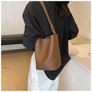 Model wearing a brown litchi pattern leather bucket bag with adjustable shoulder strap