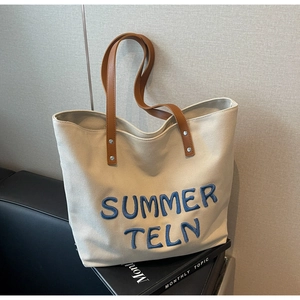 Détail du sac cabas en toile avec broderie bleue et bandoulière en cuir marron