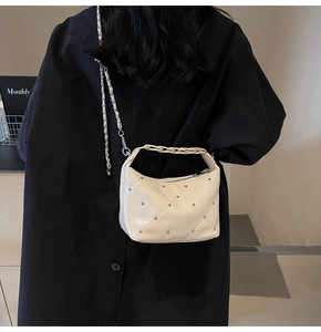 Detail of a quilted cream chain bag with silver studs worn by a model in a modern room