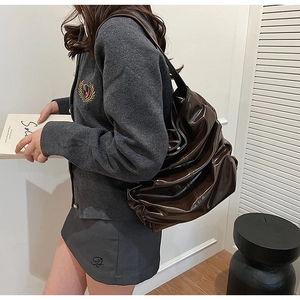 Detail of dark brown glossy synthetic leather shoulder bag with pleated texture and draping