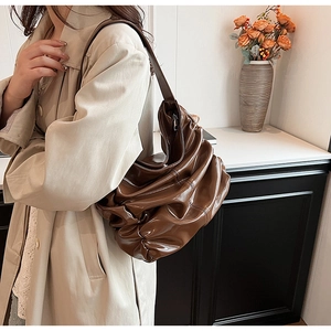 Vista laterale della borsa a spalla marrone plissettata in ecopelle con trench beige