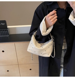 Detail of cream-white quilted handbag with silver studs and metal chain strap
