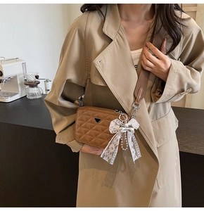 Detailed close-up of brown quilted camera bag with triangle logo and white lace bow accessory