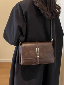 Retro dark brown crossbody bag with gold hardware worn over a black wool coat