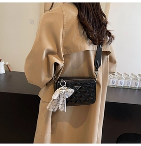 Detail of a black quilted camera bag with a wide strap and a white lace bow charm