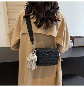 Close-up of quilted black camera bag with broad strap and lace bow charm detail