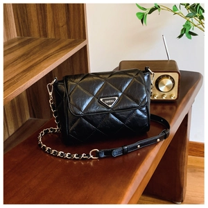 Close-up of black quilted leather texture and metallic triangle logo on crossbody bag