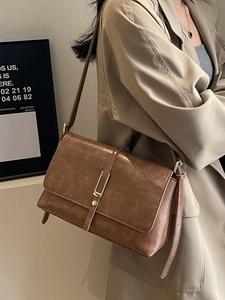Retro brown leather crossbody bag for women with gold clasp shown on a beige trench coat