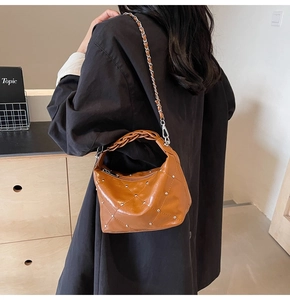 Close-up of caramel leather crossbody bag with silver rivets and woven chain strap
