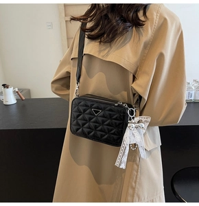 Close-up of quilted camera bag with triangle metal logo and white lace bow detail