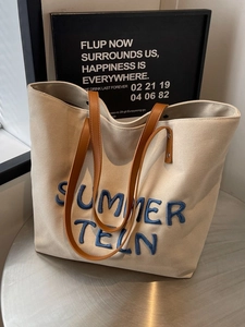 Sac cabas en toile avec bandoulières en cuir et broderie bleue sur table argent