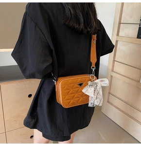 Detail of brown quilted camera bag with wide strap and white lace bow accessory